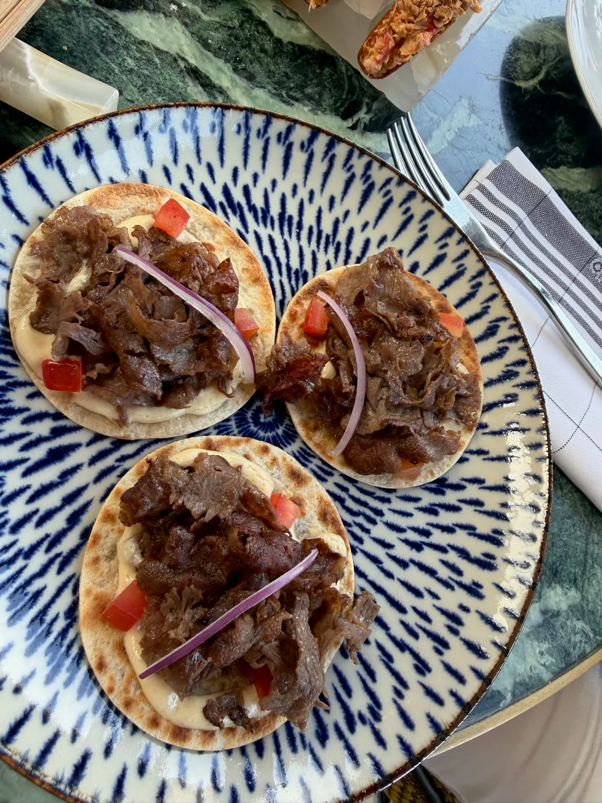 Overhead view of three Wagyu kebabs on a blue and white plate at Beefbar Monte-Carlo, with a striped napkin and cutlery beside
