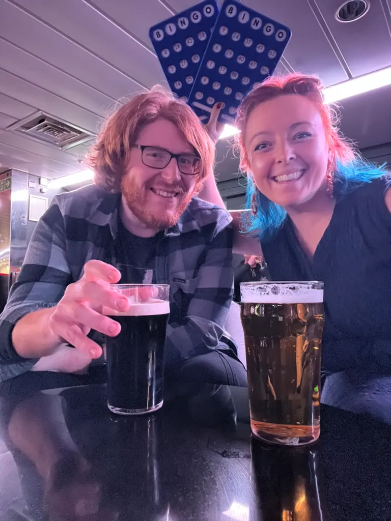The two of us at a table in the ship's bar, each with a pint, holding a pair of blue bingo boards up behind our heads.