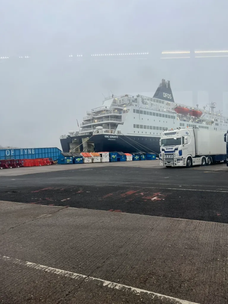 The DFDS ship King Seaways berthed at the Port of Tyne in thick fog, with a lorry and freight containers on the quayside in front of it.