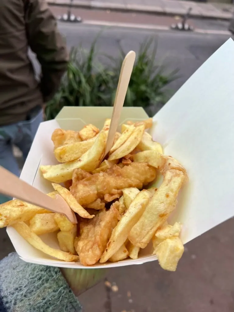 A box of battered fish and thick cut chips held up outside the chippy, two wooden forks stuck in