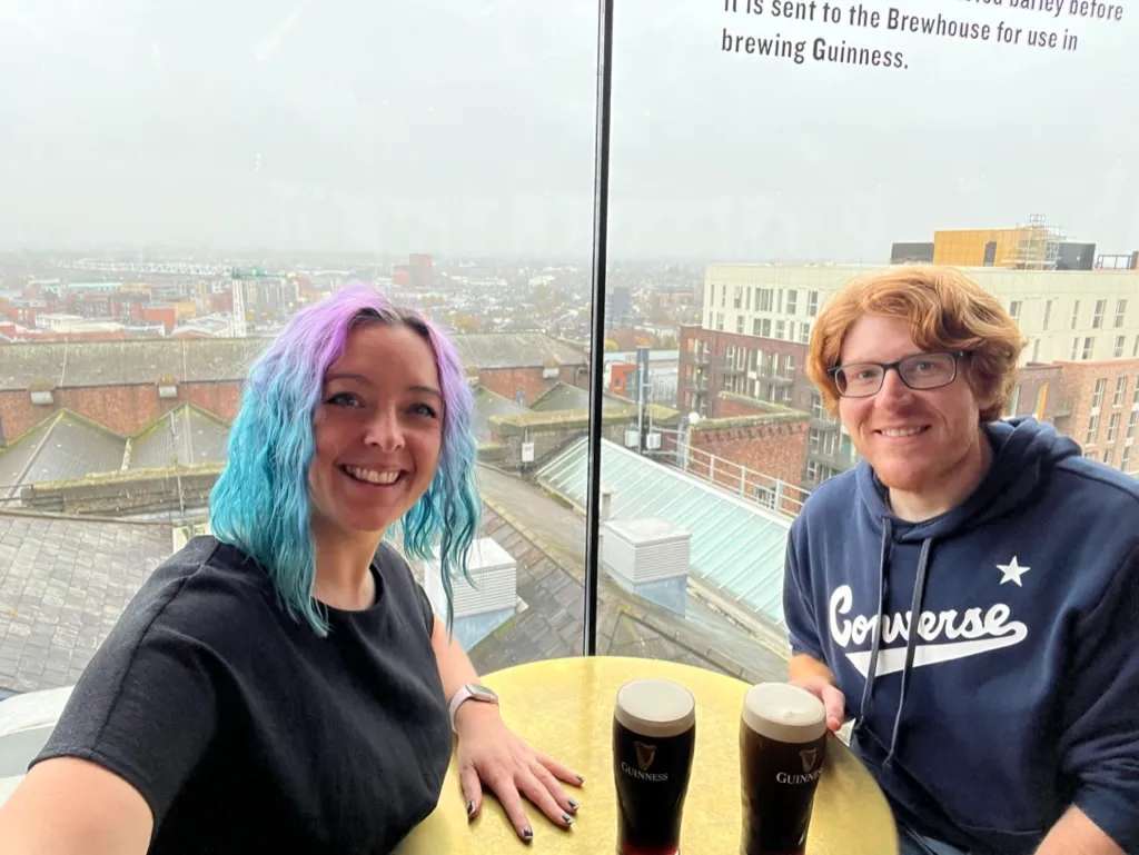 The Gravity Bar with two pints of Guinness on a yellow table and the Dublin skyline through the window