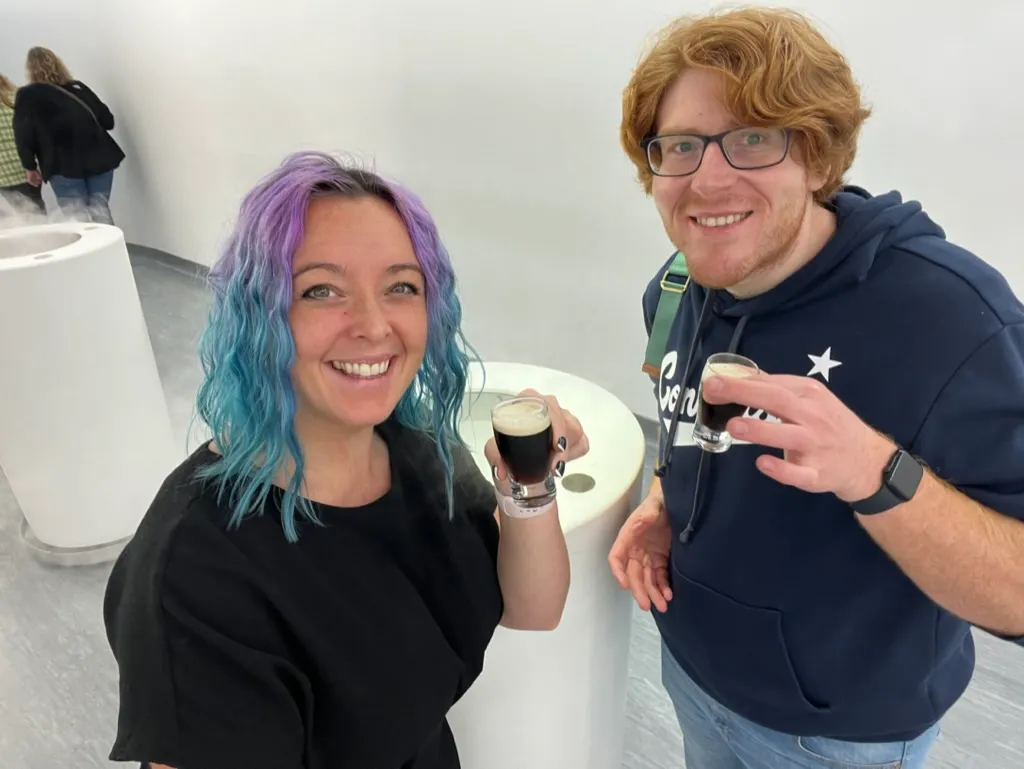 The two of us holding small tasting glasses of Guinness at a white pedestal in the Tasting Rooms
