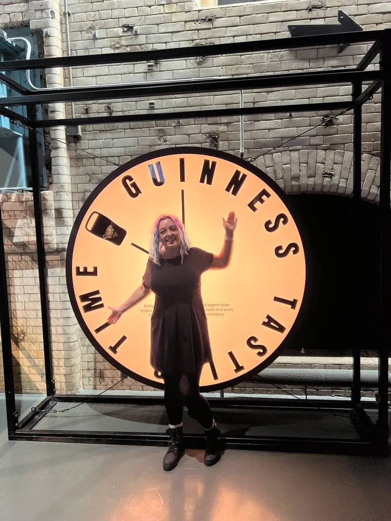 Standing arms-out in front of a giant illuminated Guinness Tasting Time clock face