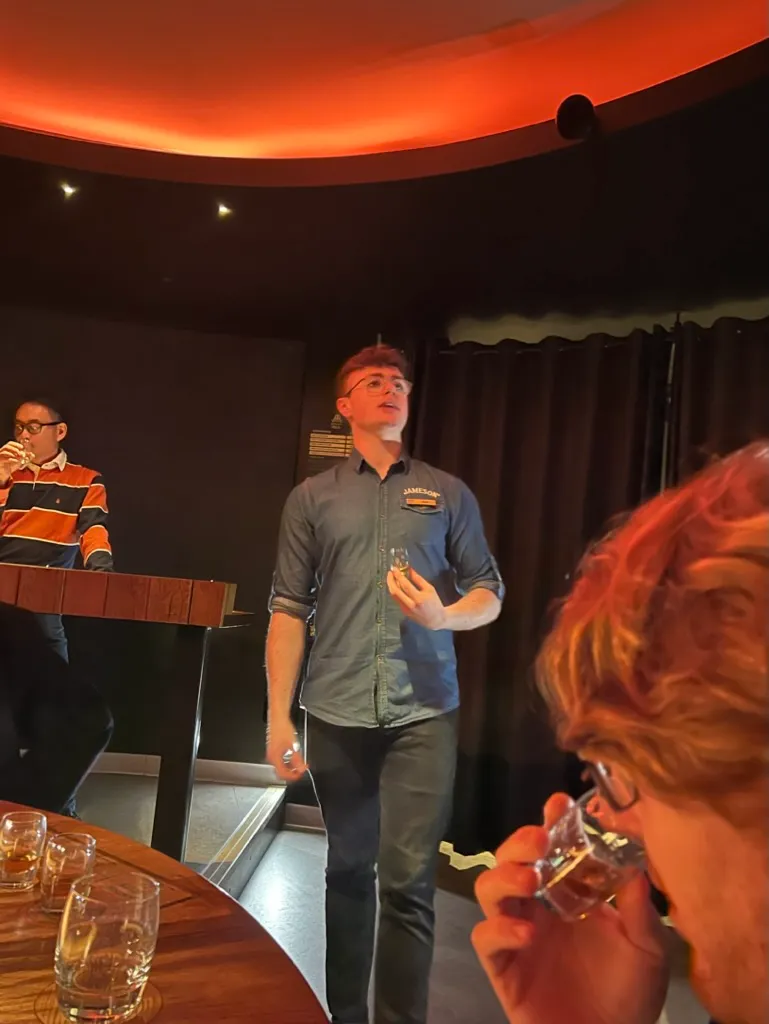 A Jameson guide talking to the group in the tasting room under orange lighting