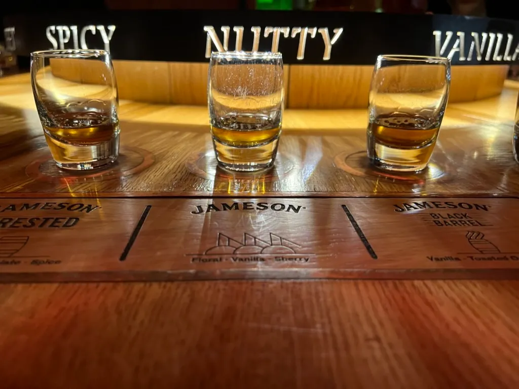 Three whiskey glasses on the Jameson tasting board, the words spicy, nutty and vanilla on the stand behind them