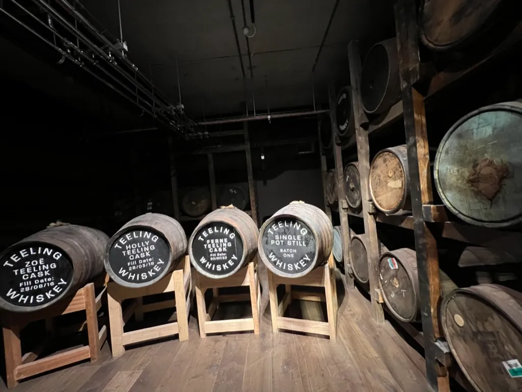 Rows of Teeling casks in the dark warehouse, four end-on in the foreground labelled Zoë, Holly, Ferne and Single Pot Still Batch One