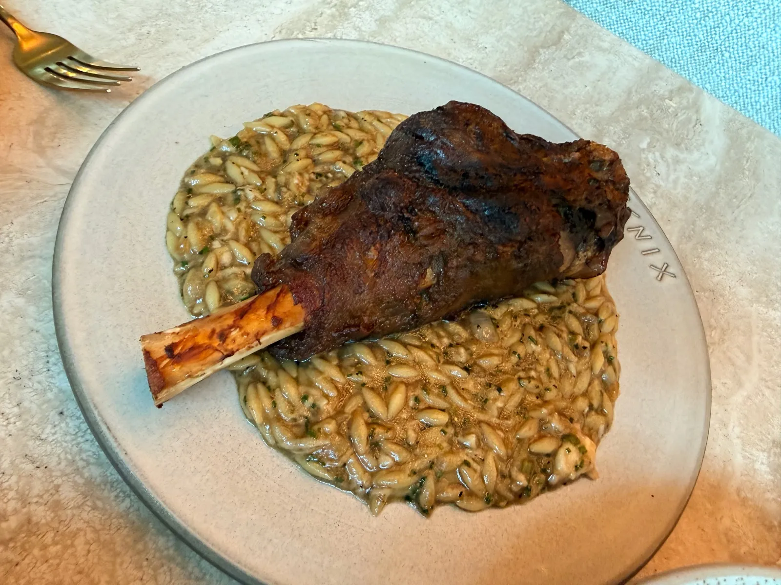 Lamb Shank Giouvetsi at Fenix Manchester, a whole braised lamb shank on the bone sitting on a bed of orzo flecked with green herbs.