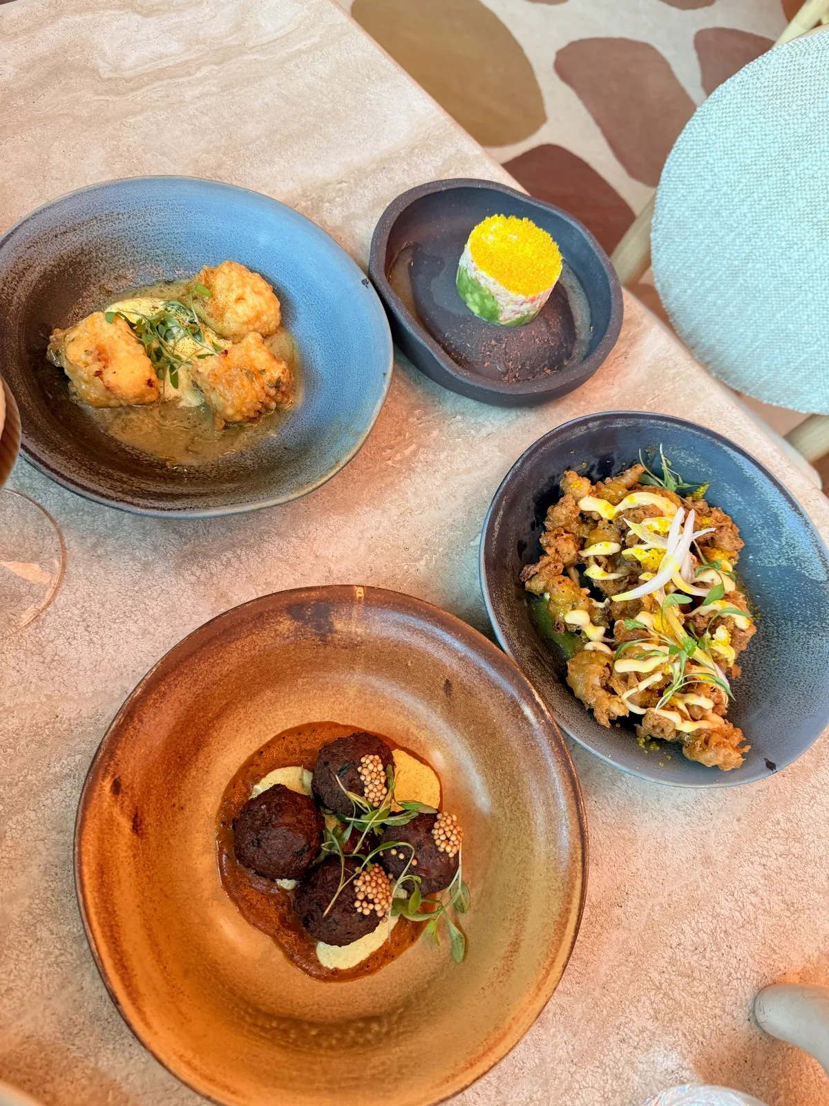 Four small plates at Fenix Manchester: halloumi tempura in a green sauce, a truffle crab salad tower in a dark dish, fried calamari with a yellow drizzle, and four spicy meatballs on a pale yoghurt, all scattered with tiny green micro herb leaves.