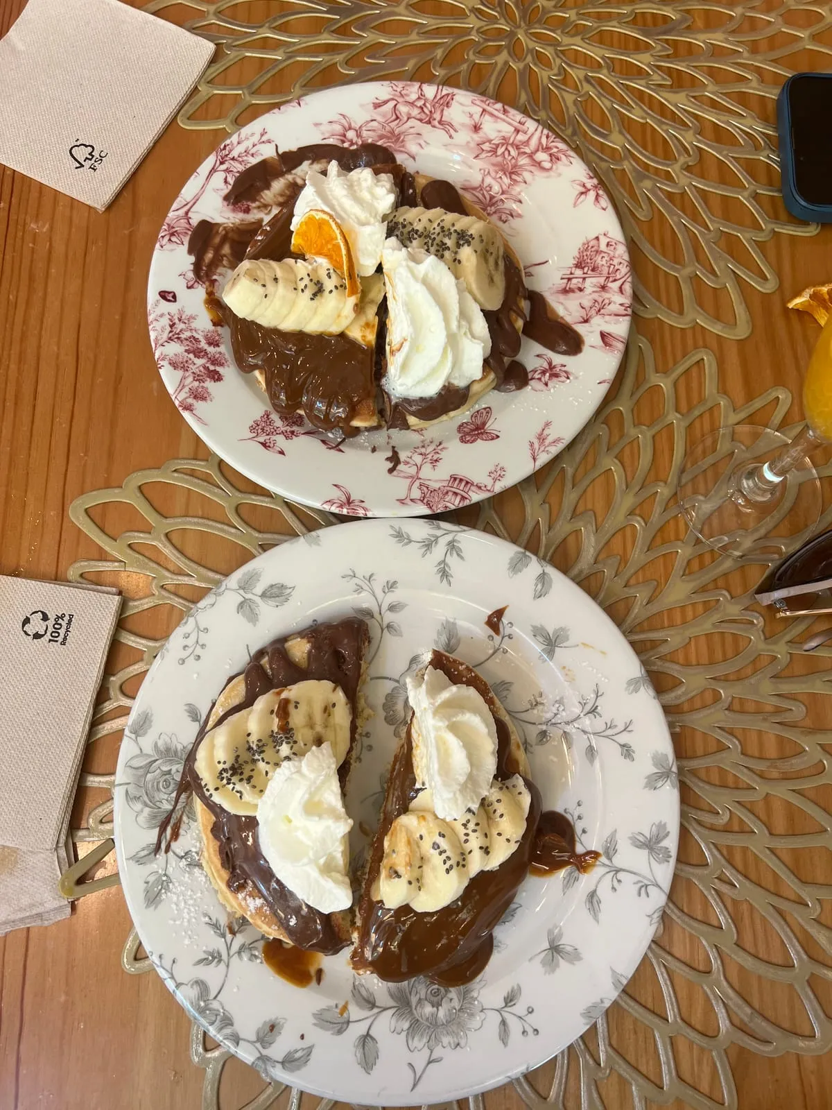 Two plates of pancakes at The Florentine, Barcelona: the dolce topped with caramel sauce, cream and a dried orange slice, and the banana Nutella with cream, sliced banana and chia seeds