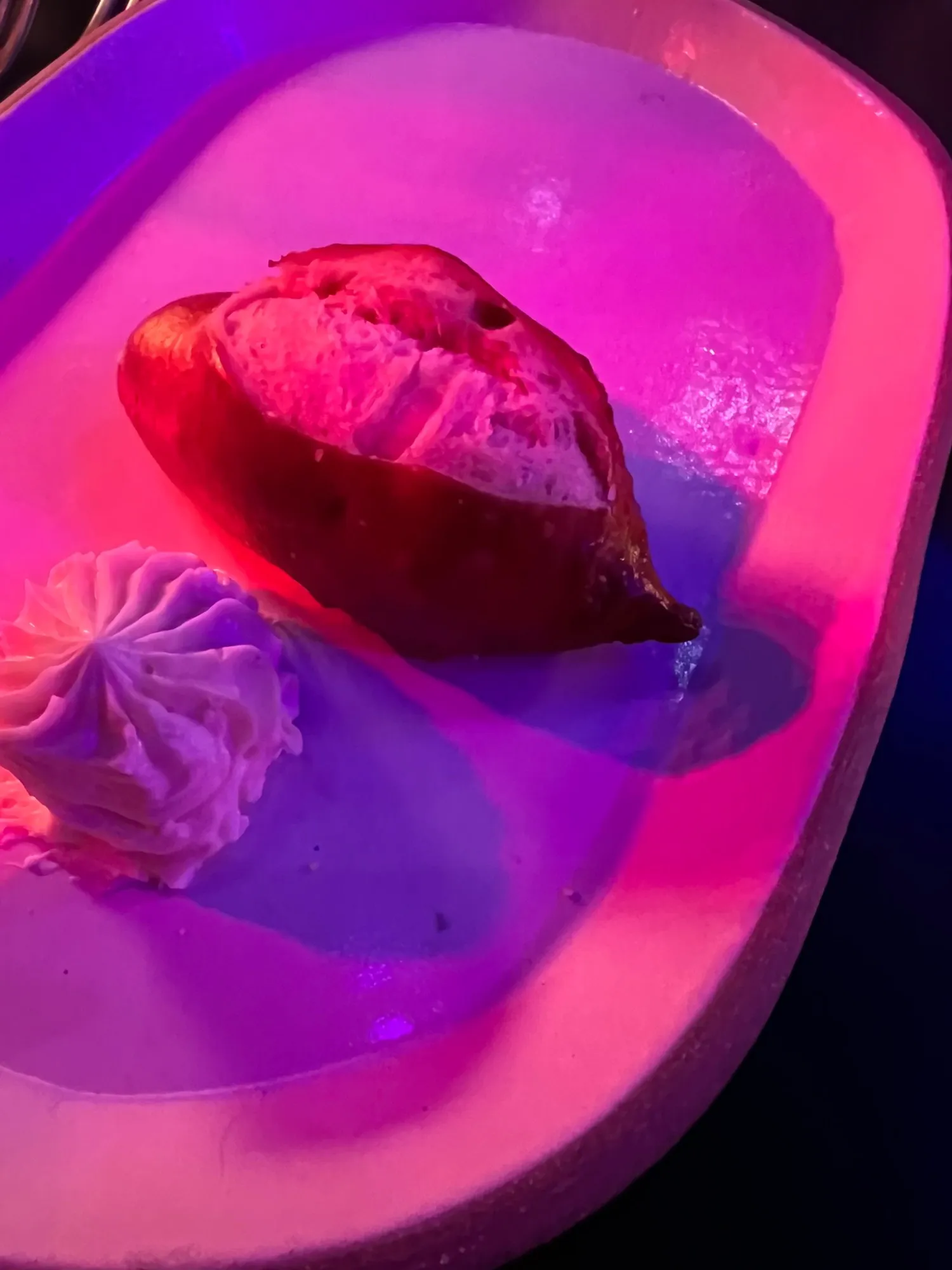 A dessert lit up in pink and purple club lighting, with a swirl of cream alongside.