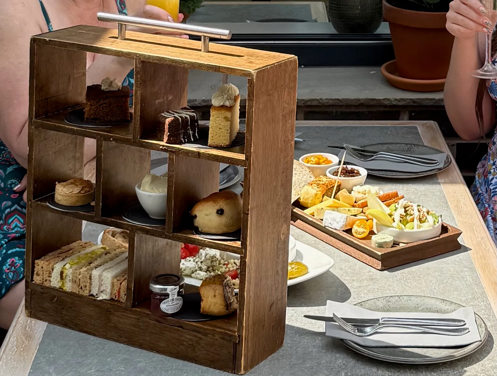 Afternoon tea at The Manor House Alsager served in a wooden shelving unit, sandwiches on the bottom shelf, scone and tart in the middle and cakes on top, with the ploughman's board alongside