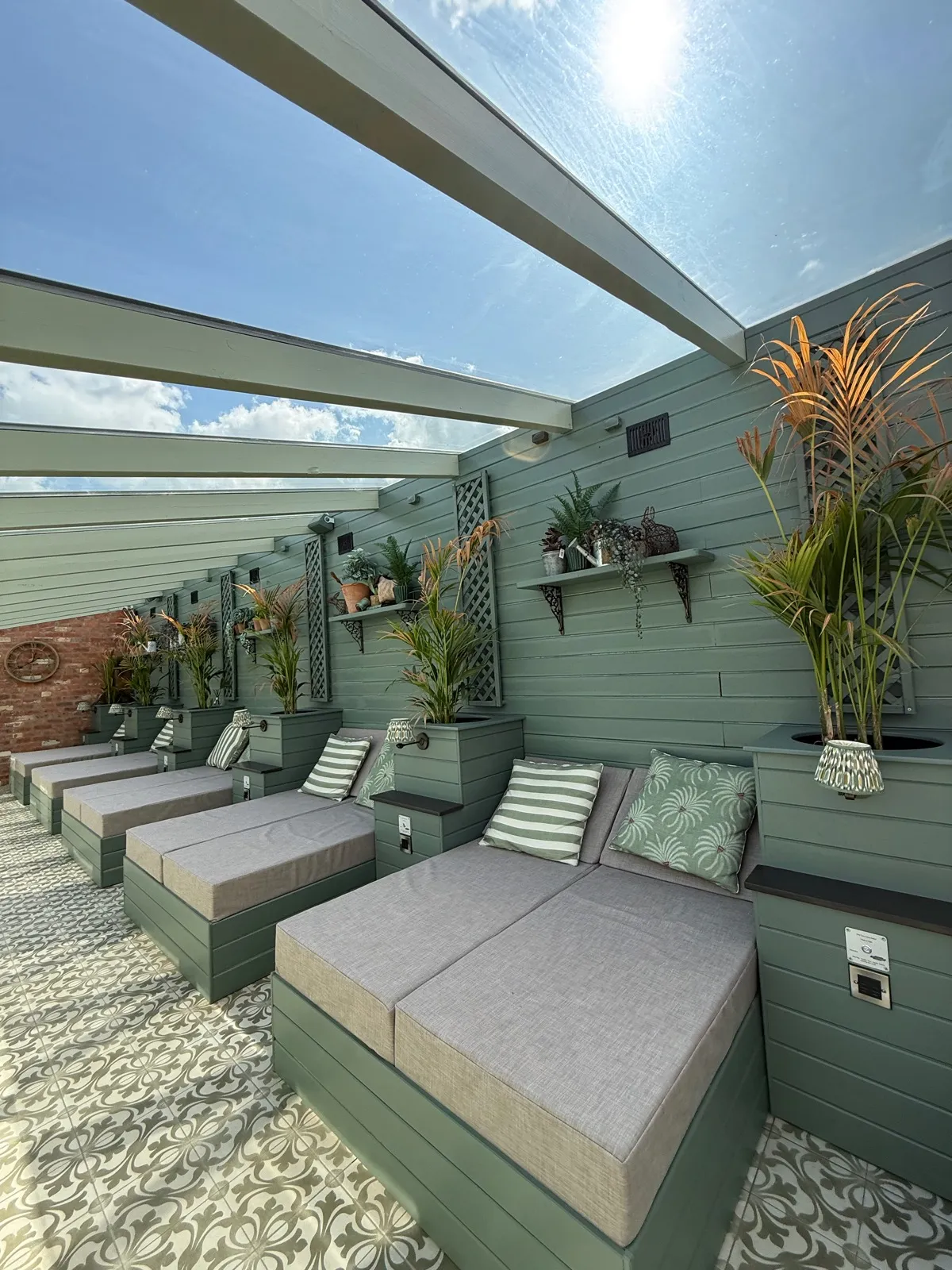 A covered lounging area at The Manor House Alsager, sage green panelling with a glass roof, grey double loungers and patterned encaustic floor tiles