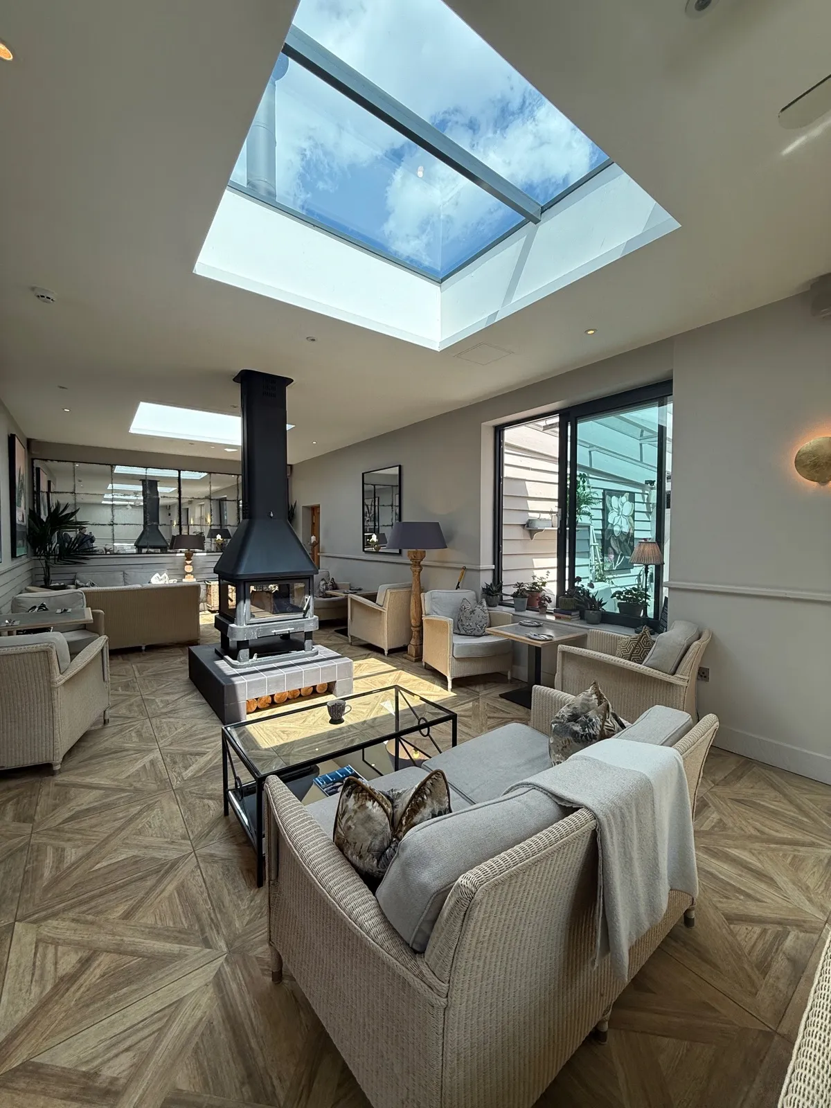 The indoor spa lounge at The Manor House Alsager, wicker armchairs around a suspended central fireplace under two large skylights