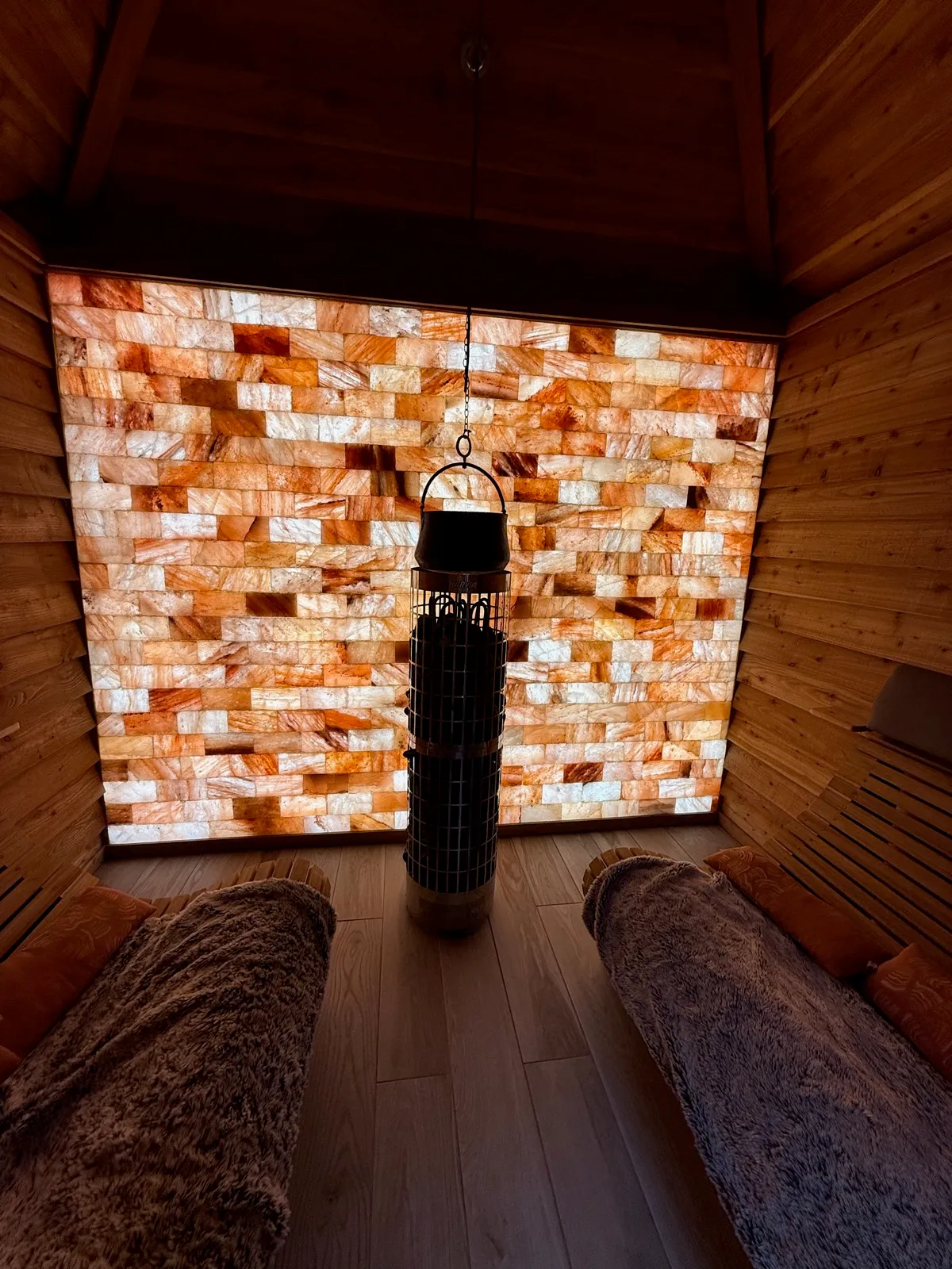 The salt sauna at The Manor House Alsager, a wall of backlit Himalayan salt brick behind a central stove, with fur throws over the benches
