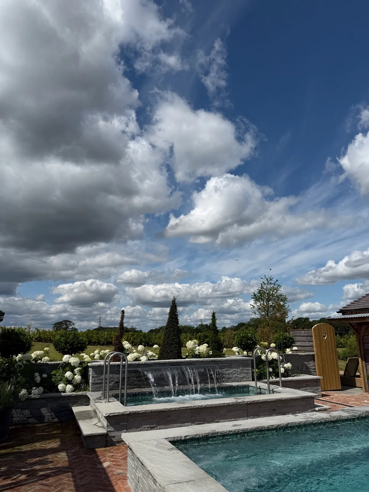 The outdoor spa pool at The Manor House Alsager, water spouts running into it, banked with white hydrangeas and looking out over open Cheshire countryside