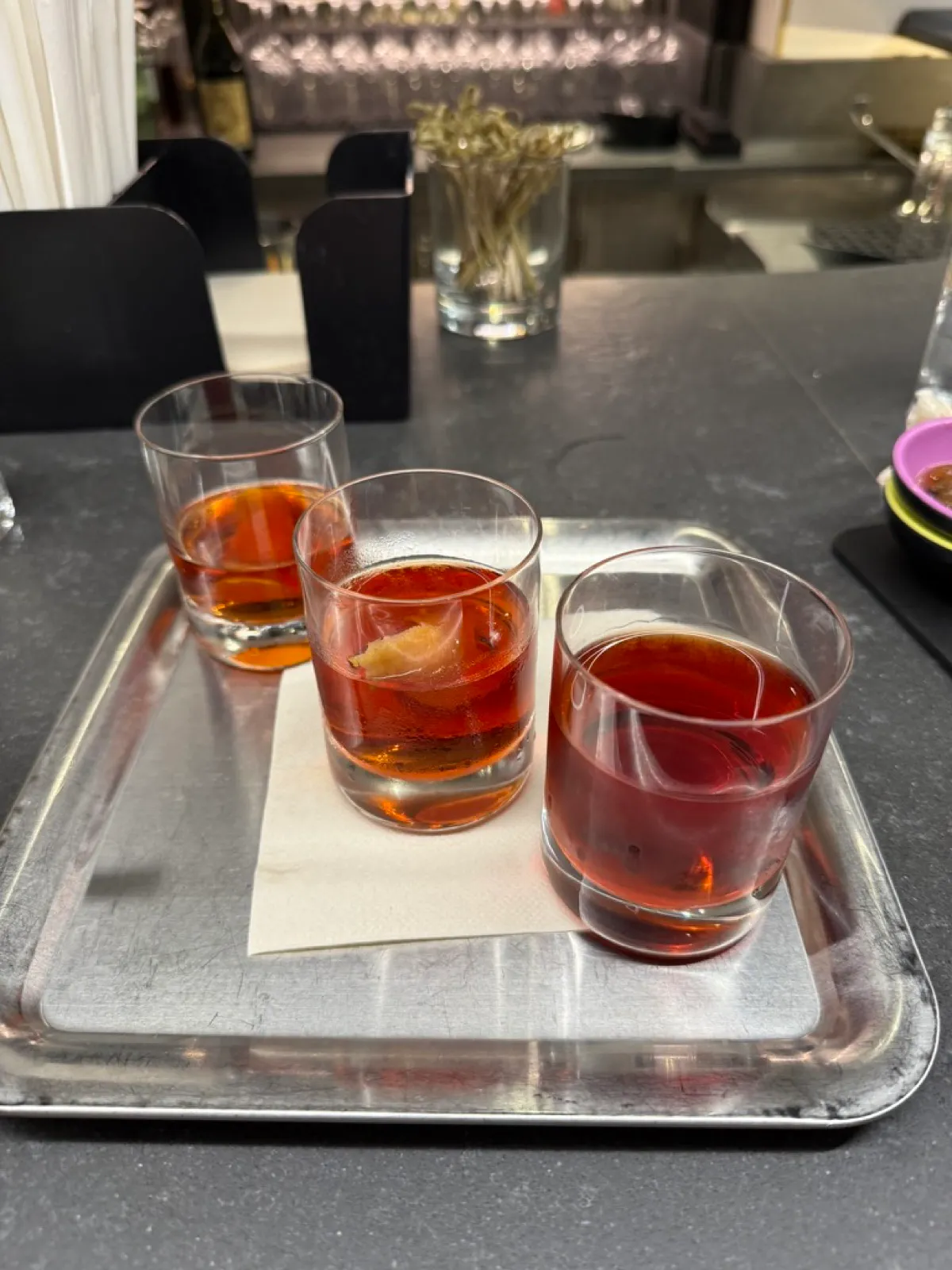 A flight of three Negronis, light, classic and bourbon, on a tray on a Virgin Voyages bar