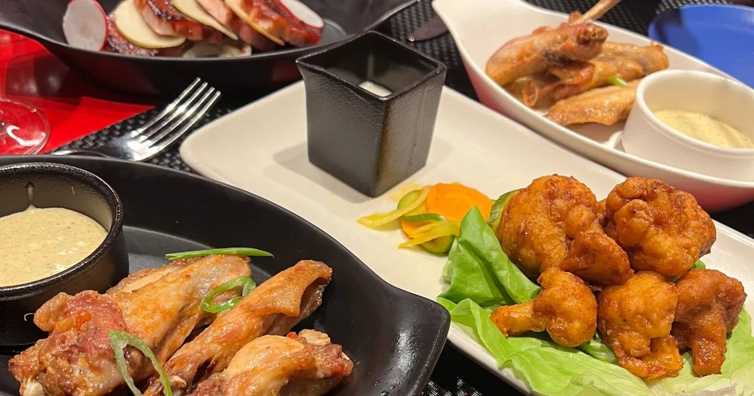 A spread of Razzle Dazzle starters on a red table: chicken wings with dip, maple pork belly bites and Nashville hot cauliflower