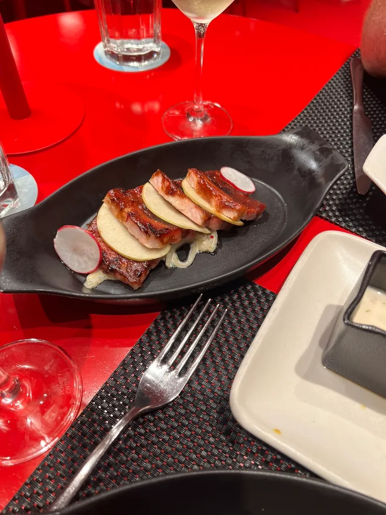 Close up of the maple glazed pork belly bites on a black dish, layered with thin apple slices and radish.