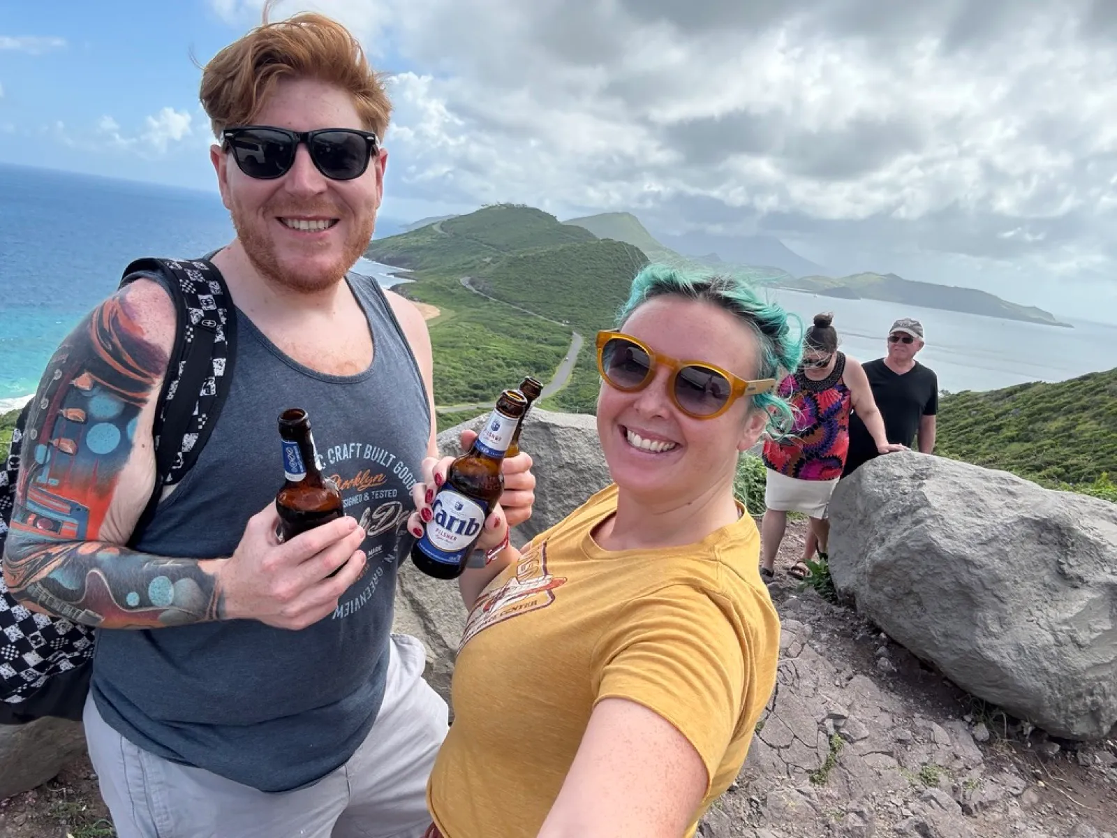 The two of us holding cold Carib beers at a hilltop viewpoint over the Southeast Peninsula of St Kitts