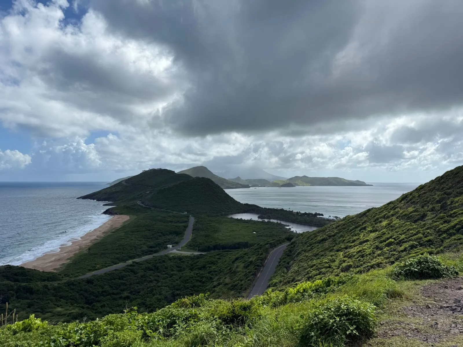 The view over the Southeast Peninsula of St Kitts from a hilltop viewpoint, with the road winding between two bays and Nevis in the distance