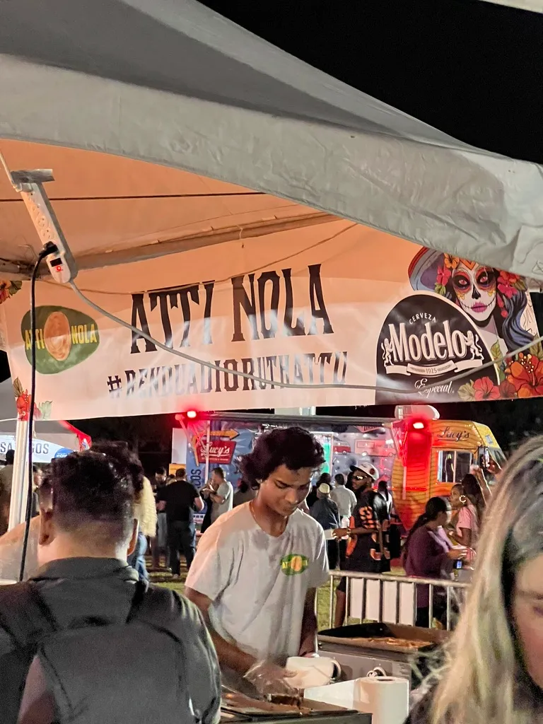 The ATL NOLA tent at night, a young man in a white t-shirt working at the counter with a crowd behind him