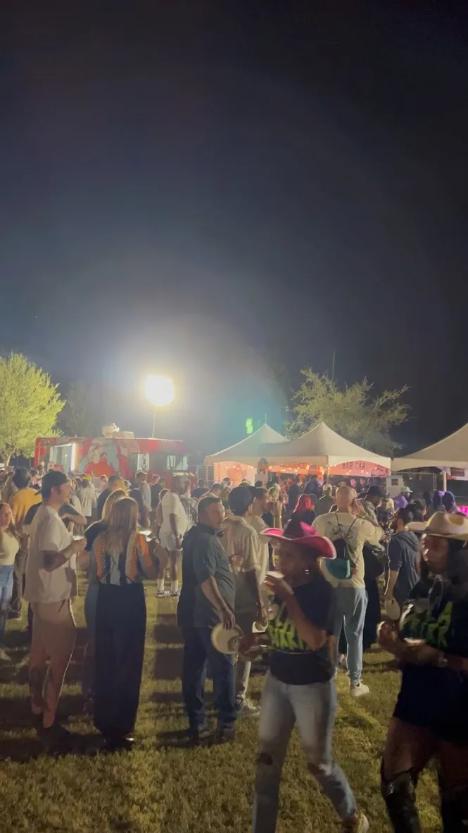 A dense crowd at the festival at night, cowboy hats, a red food truck and lit tents behind them