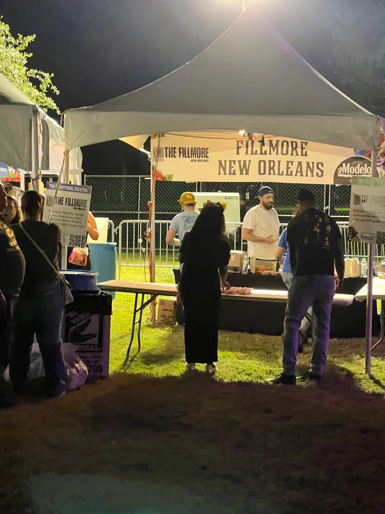 The Fillmore New Orleans tent at night, staff behind a serving table with printed signs either side listing their taco and their cocktail