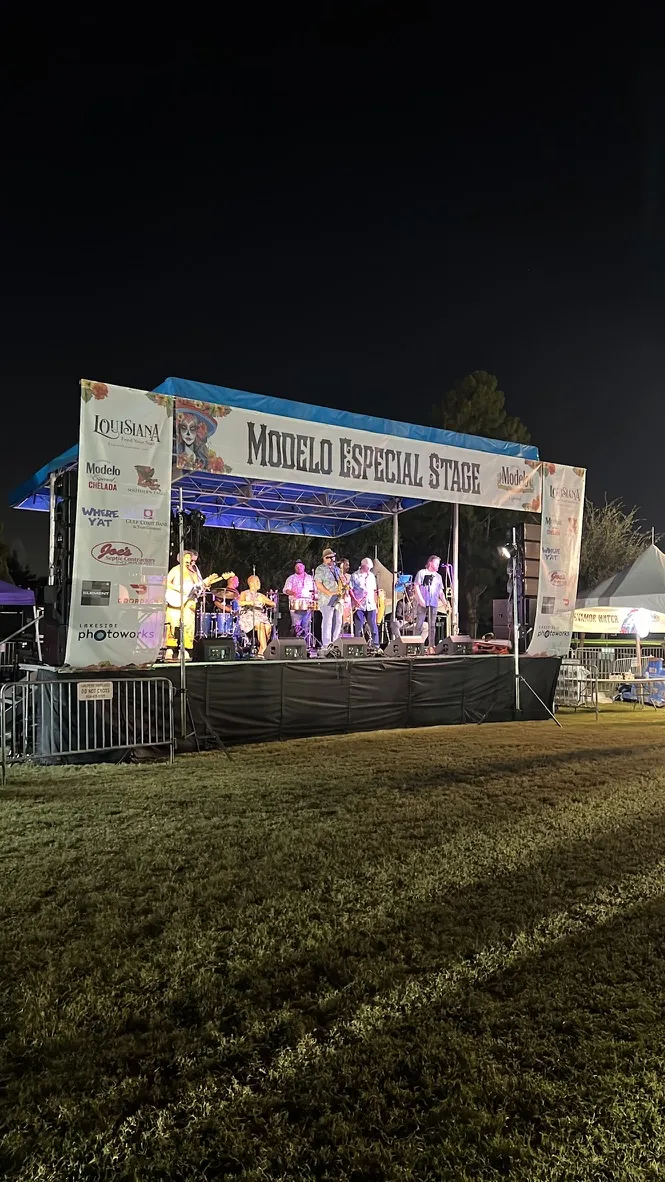A band playing under the Modelo Especial Stage banner at night, lit blue, with sponsor boards down both sides