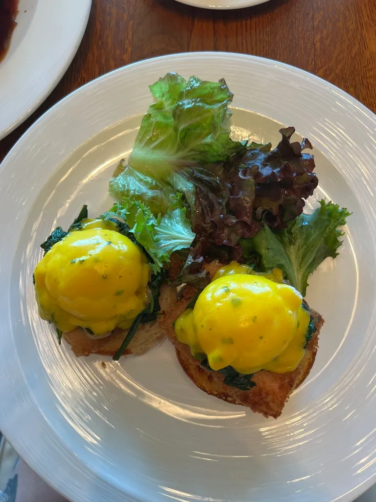 The Wake Benedict: two poached eggs under bright yellow hollandaise on toasted brioche with spinach, with a pile of dressed salad leaves alongside.