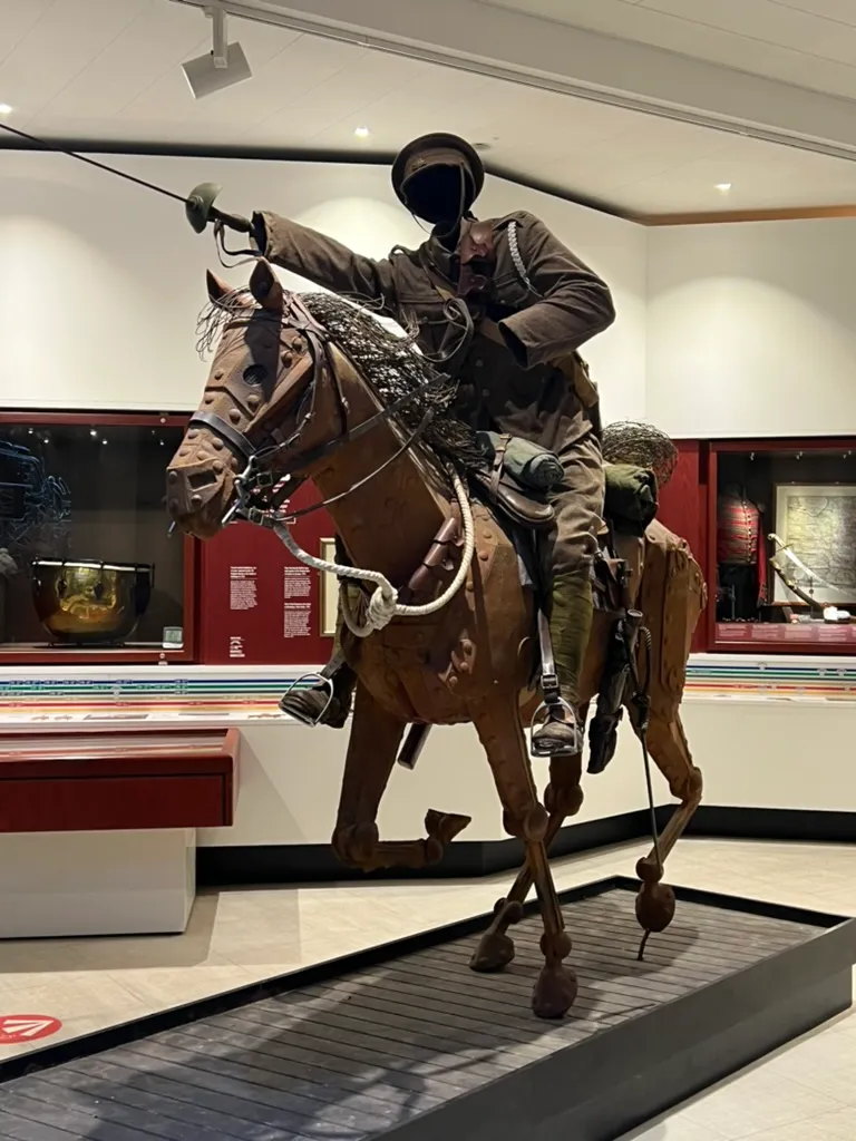 A full-size model of a First World War cavalry horse and rider mounted mid-gallop in the York Army Museum, barbed wire and display cases behind
