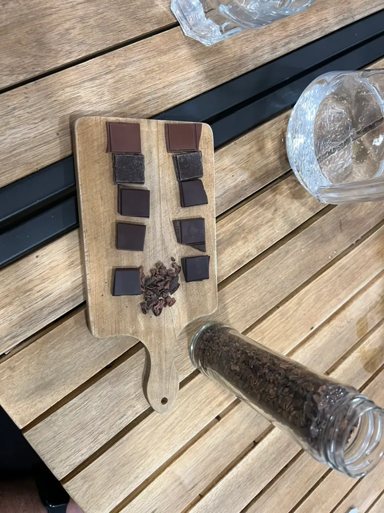 The tasting board from above, two columns of chocolate squares running from milk to dark with a heap of cocoa nibs between them and a jar of nibs tipped over beside it