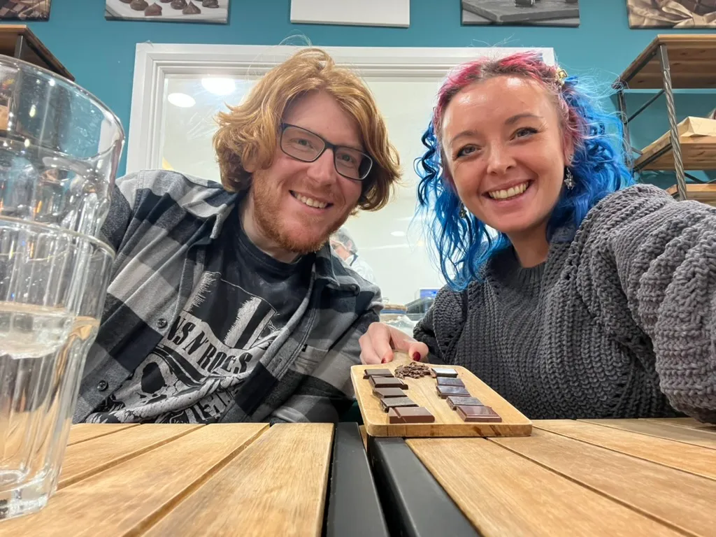 The two of us leaning over a wooden tasting board of chocolate squares with a pile of cocoa nibs in the middle