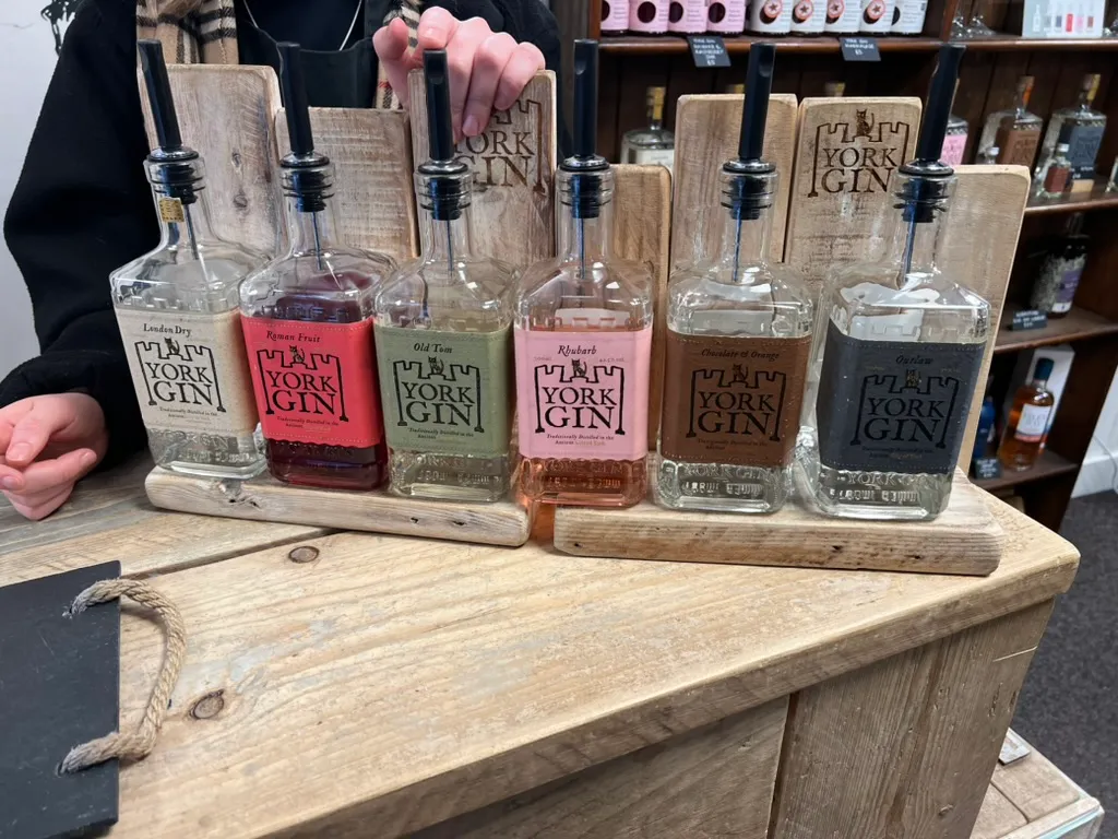 Six York Gin bottles with pourers in, lined up on wooden tasting boards along a counter, the labels reading London Dry, Roman Fruit, Old Tom, Rhubarb, Chocolate & Orange and Outlaw