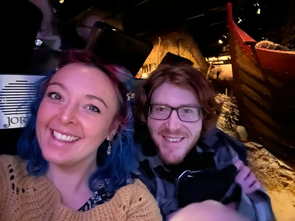 The two of us in the time capsule with a red-painted Viking boat and a thatched roof behind us