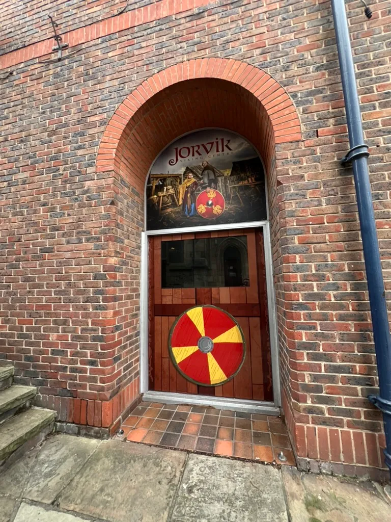 The arched brick entrance to JORVIK Viking Centre, a round red and yellow Viking shield mounted on the wooden door beneath the JORVIK sign